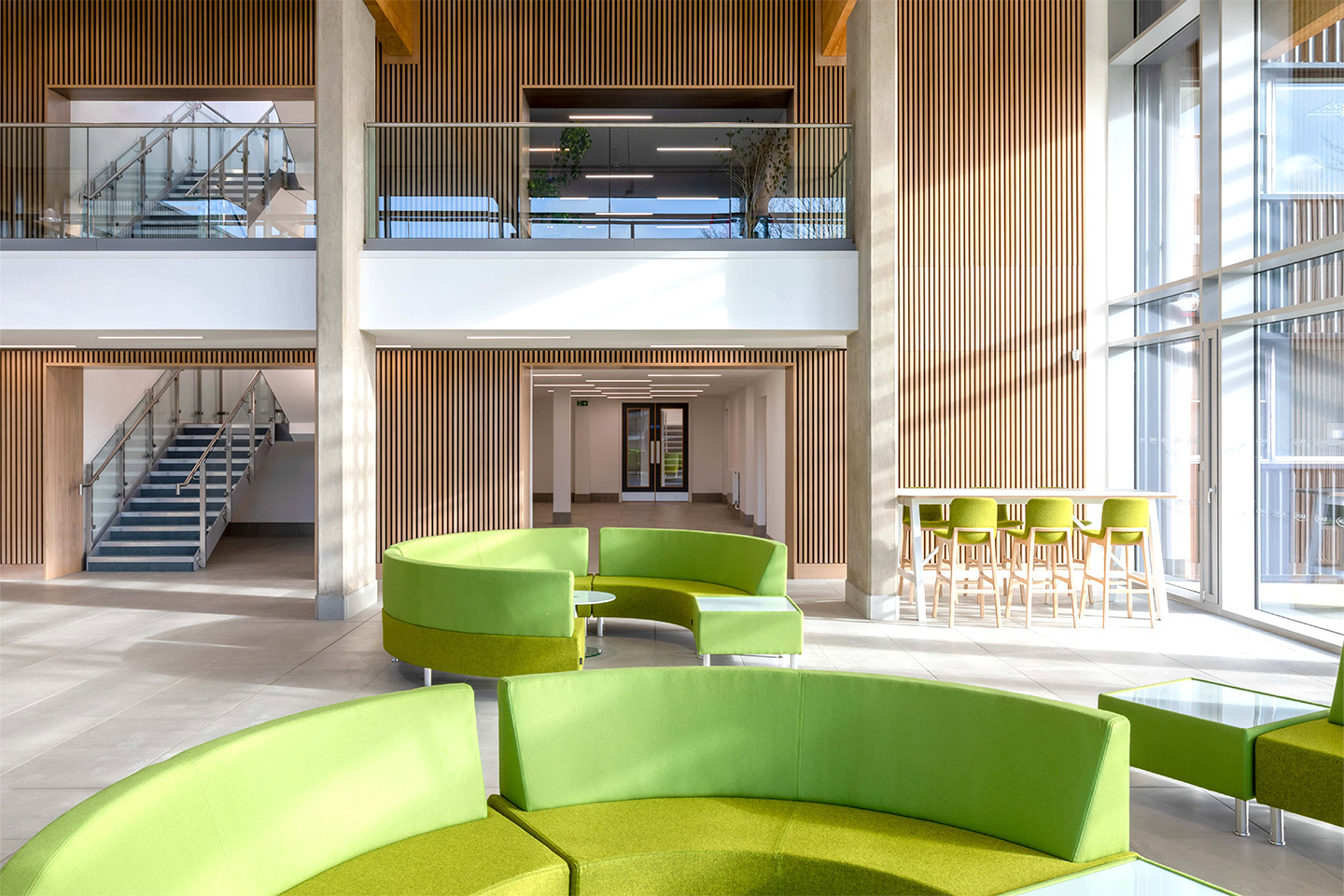 NIAB building Cambridge, entrance interior showing tall ceiling heights, panelled walls and lime green circular lounge sofas.