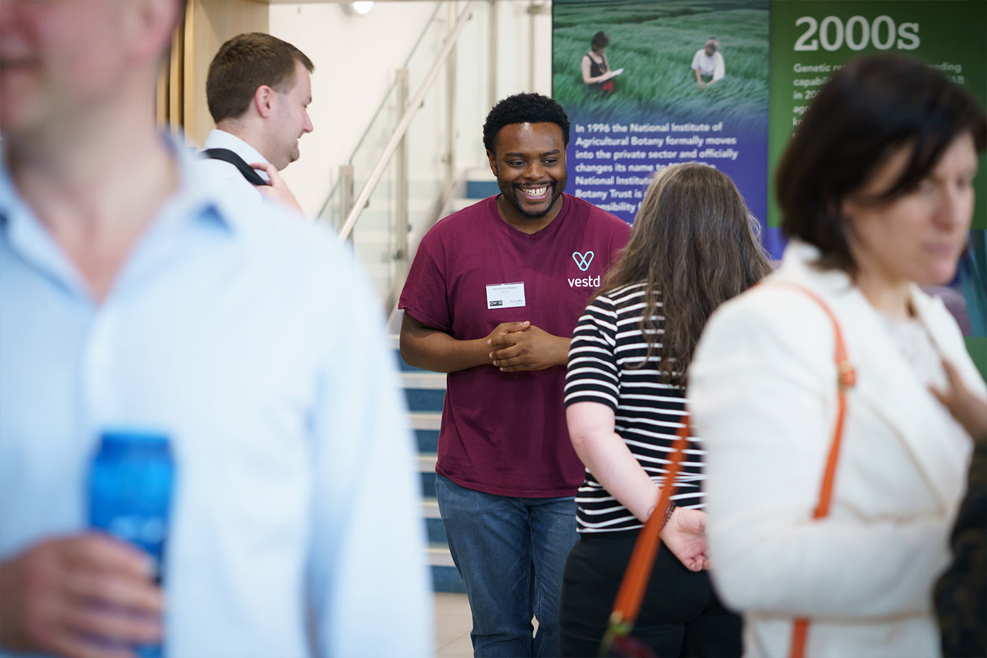 Guests talking and smiling in a bright open space while standing in front of information banners in the foyer of the NIAB building in Cambridge, UK.