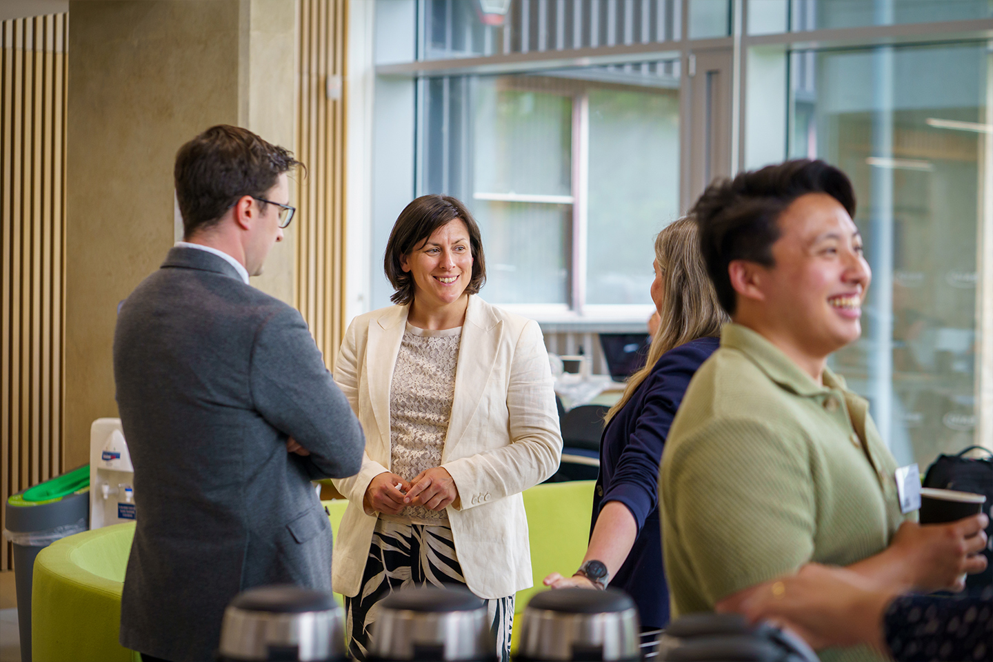 People talking and smiling in a bright open reception spaces during an event at the NIAB building in Cambridge, UK.